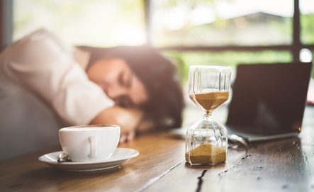 Close up of sandglass with business woman tired from working with laptop computer background. Relax Sleeping and taking nap concept. Business people and overtime workload theme. Office and home theme